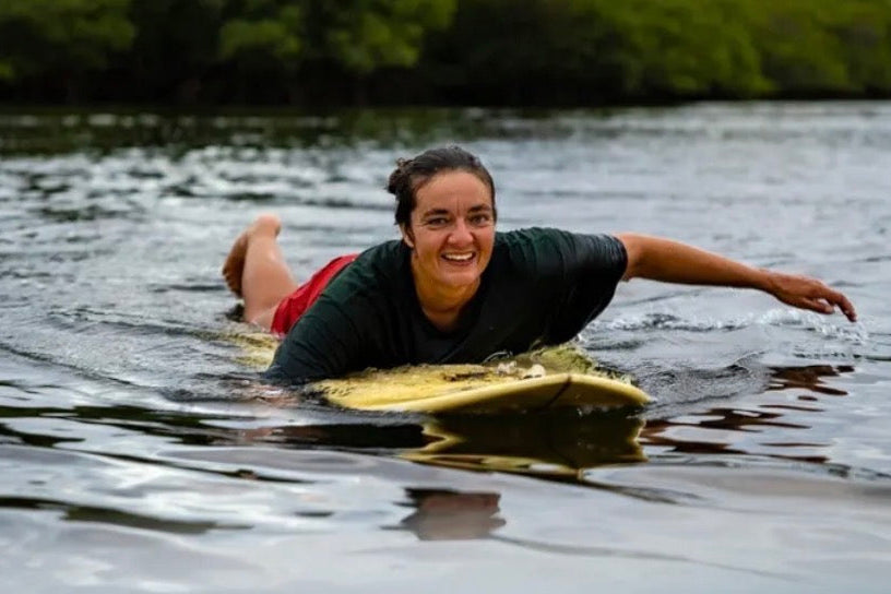 Person lying on a surfboard in water with a scenic background