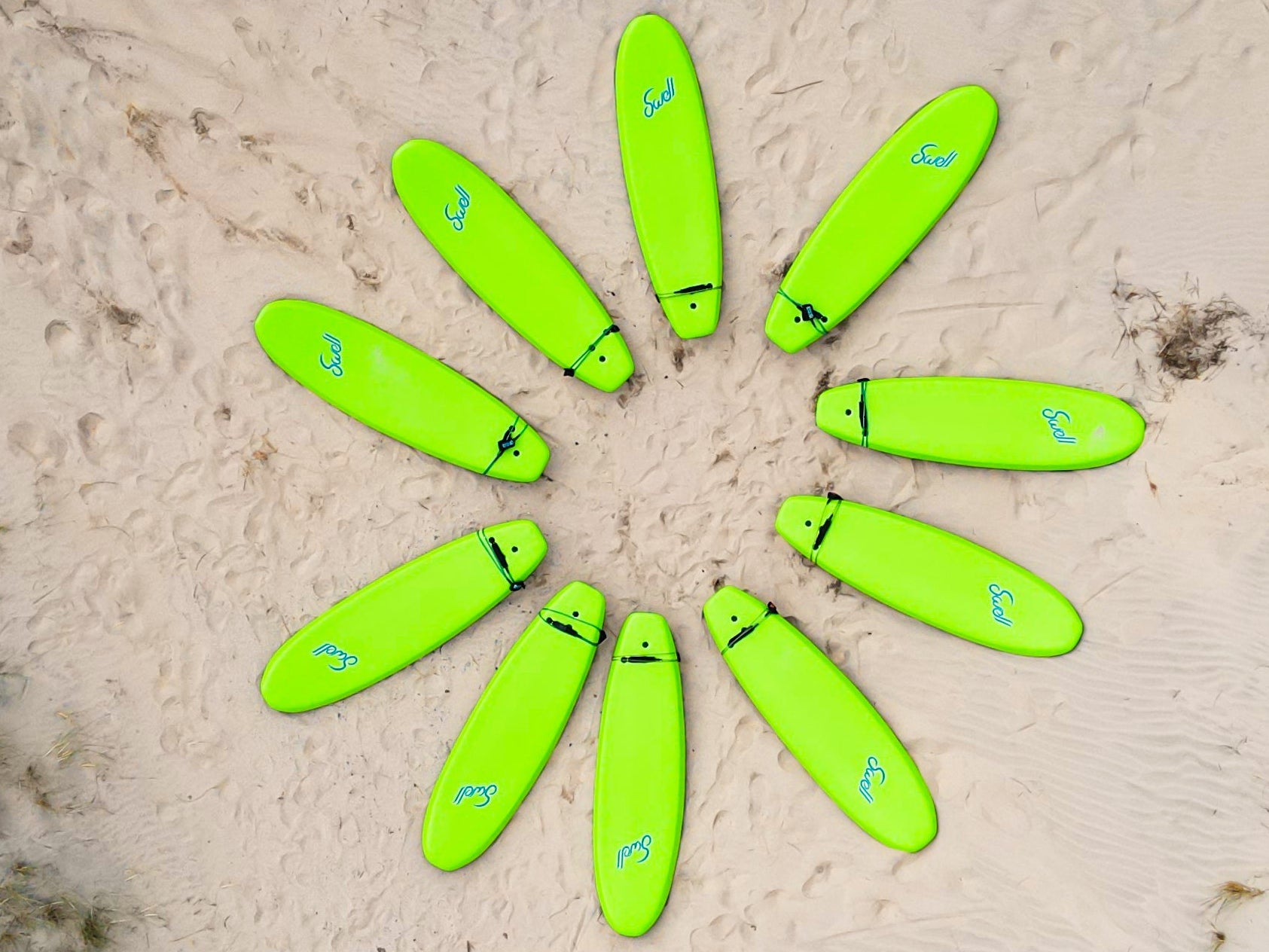 A circle of green surfboards on a sandy beach with grassy areas.